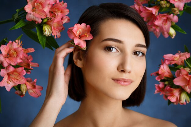 Close up portrait of tender  young woman with flowers over blue wall