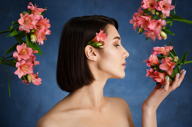 Free photo close up portrait of tender  young woman with pink flowers over blue wall