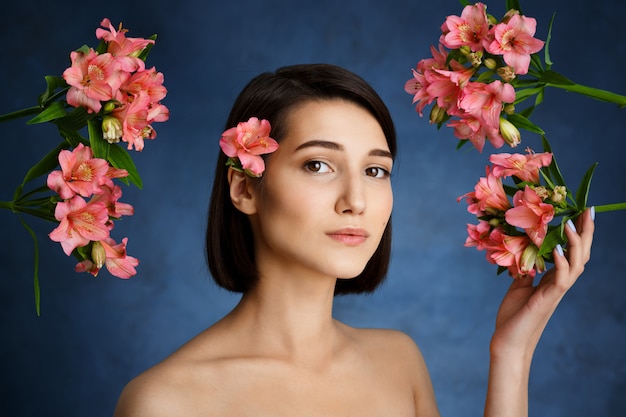 Close up portrait of tender  young woman with pink flowers over blue wall