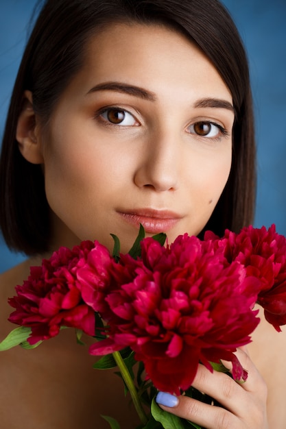 Close up portrait of tender  young woman with red flowers over blue wall