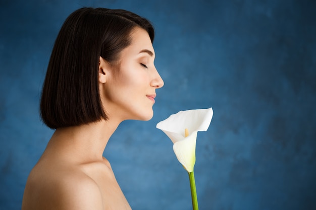 Free photo close up portrait of tender  young woman with white flower over blue wall