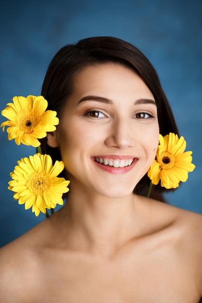 Close up portrait of tender  young woman with yellow flowers over blue wall