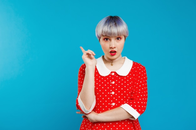 Free photo close up portrait upset beautiful dollish girl with short light violet hair wearing red dress over blue wall