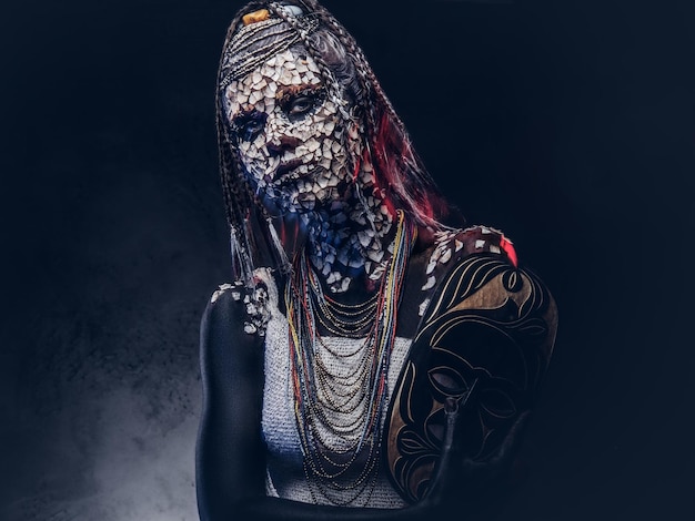 Close-up portrait of a witch from the indigenous African tribe, wearing traditional costume. Make-up concept. Isolated on a dark background.