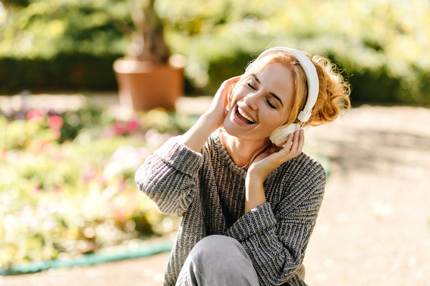 Free photo close-up portrait of woman listening to music in good mood, dressed in gray knitted sweater.