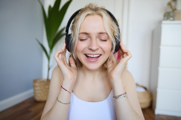 Free Photo close up portrait of woman smiling while listening to music in wireless headphones singing with eyes