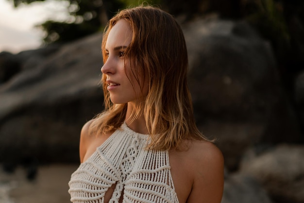 Close up portrait of woman  in white boho crochet dress posing on the beach. Summer and tropical vacation fashion photo.