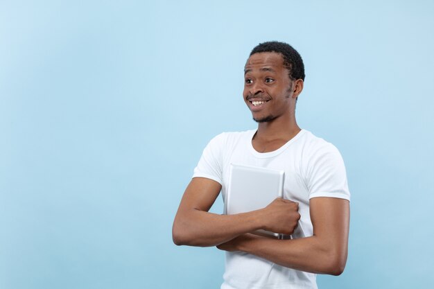 close up portrait of young african-american man in white shirt. Human emotions, facial expression, ad, sales concept. Holding a tablet and smiling. Looks happy.