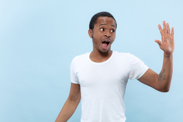 close up portrait of young african-american man in white shirt. Human emotions, facial expression, ad, sales concept. Meeting somebody, greeting, inviting.