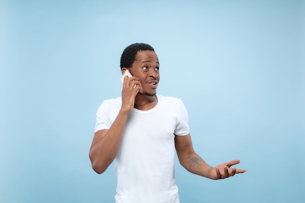 close up portrait of young african-american man in white shirt.. Talking on the phone, holding a smartphone.