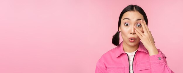 Close up portrait of young asian girl looking surprised express amazement and wonder peeking through