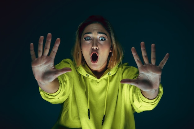 Close up portrait of young crazy scared and shocked caucasian woman isolated on dark background.