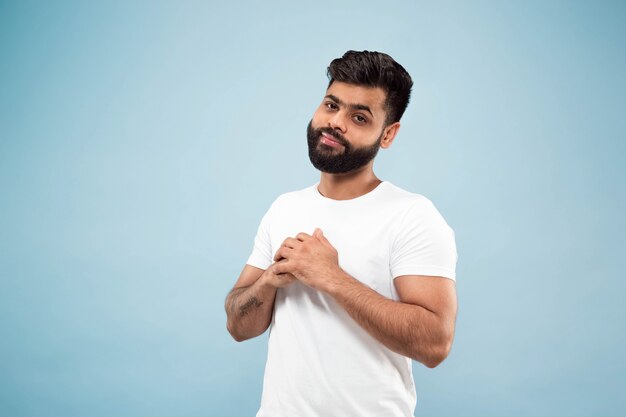 close up portrait of young indian man in white shirt.  Posing, standing and smiling, looks calm.