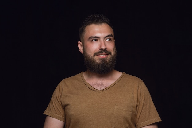 Free photo close up portrait of young man isolated on black studio background. photoshot of real emotions of male model. dreaming and smiling, hopeful and happy. facial expression, human emotions concept.