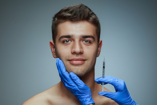 Close-up portrait of young man isolated on grey  background. Filling surgery procedure.