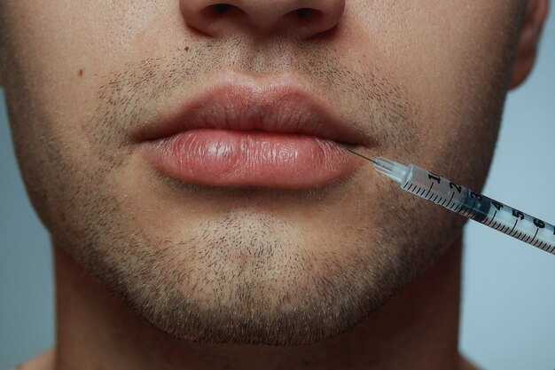 Close-up portrait of young man isolated on grey  background. Filling surgery procedure.