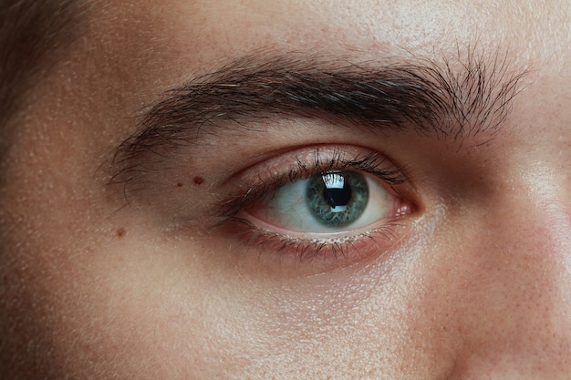 Close-up portrait of young man isolated on grey studio background. Caucasian male model's face and blue eye. Concept of men's health and beauty, self-care, body and skin care, medicine or phycology.