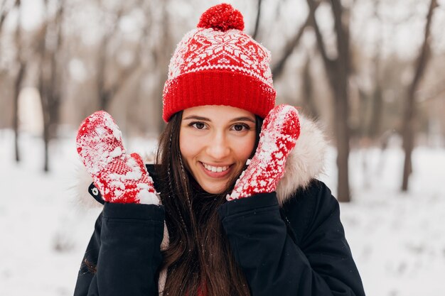 Close up portrait of young pretty candid smiling happy woman in red mittens and knitted hat wearing fur coat walking playing in park in snow, warm clothes, having fun