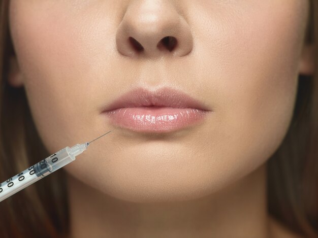 Close-up portrait of young woman on white  wall. Filling surgery procedure. Lip augmentation. Concept of women's health and beauty, cosmetology, self-care, body and skin care. Anti-aging.