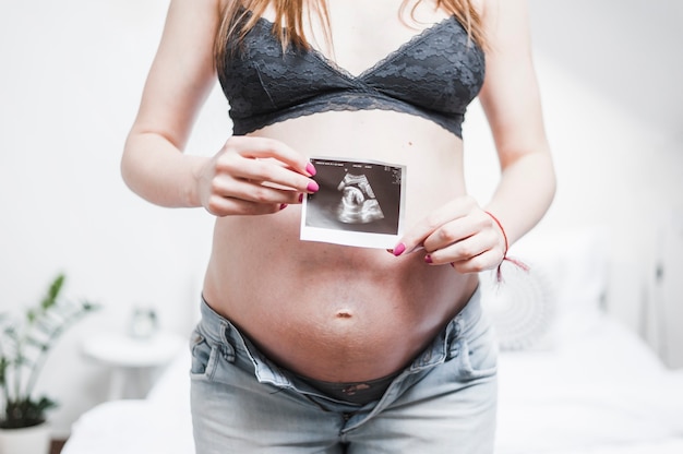 Close-up of a pregnant woman holding ultrasound photo in front of her belly