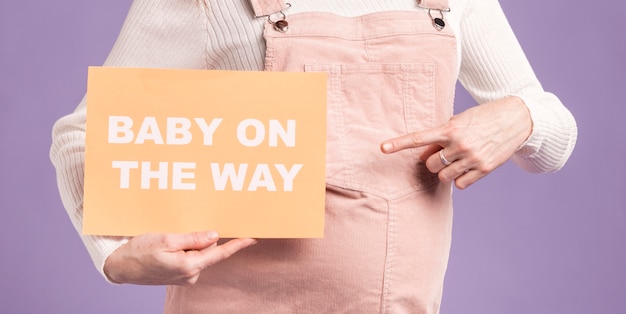 Close-up pregnant woman pointing at paper with baby on the way message