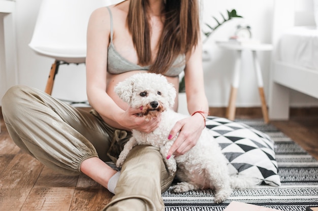 Free photo close-up of pregnant woman with her lovely white toy poodle sitting on floor