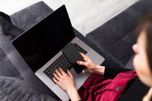 Close up. Pretty brunette using phone and laptop at home in the living room