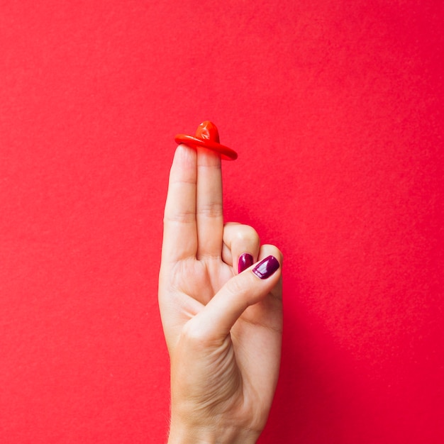 Free photo close-up red condom on woman's fingers