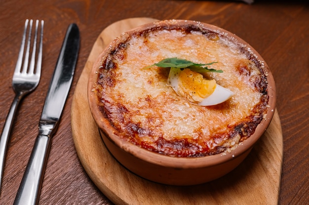 Close up of roasted italian dish in pottery pan garnished with melted cheese and boiled egg halve