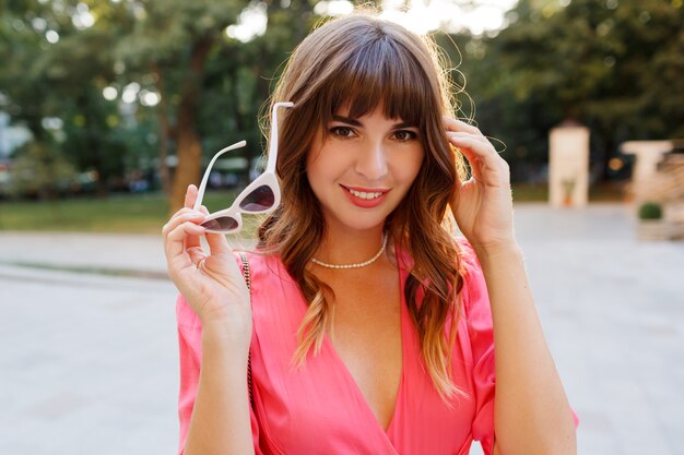 Close up s portrait of elegant fashionable woman  with wavy hairs in romantic  pink dress posing in city center, Sunset colors.