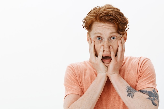 Free photo close-up of scared insecure redhead man holding hands on face shocked, gasping startled