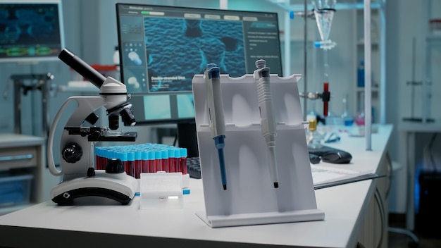 Free photo close up of scientific micropipette and instruments in chemical laboratory. medical desk in empty room with vacutainers, test tubes, glass samples, microscope and dna animation on computer