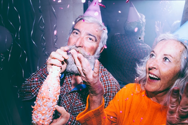 Close-up of senior man holding champagne bottle and her wife throwing confetti in air at birthday party