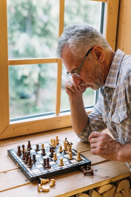 Free Photo close-up of senior man playing chess on window sill