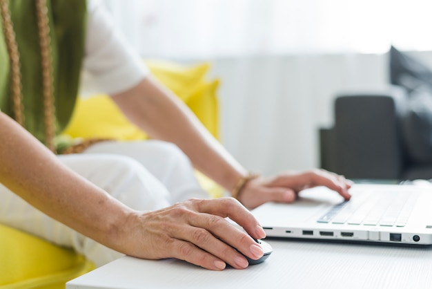 Free photo close-up of senior woman's hand using mouse and laptop