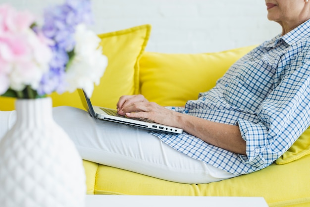 Free photo close-up of senior woman sitting on sofa typing on laptop