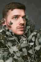 Free photo close-up of a serious young man with pierced ears and nose covered with dry green leaves