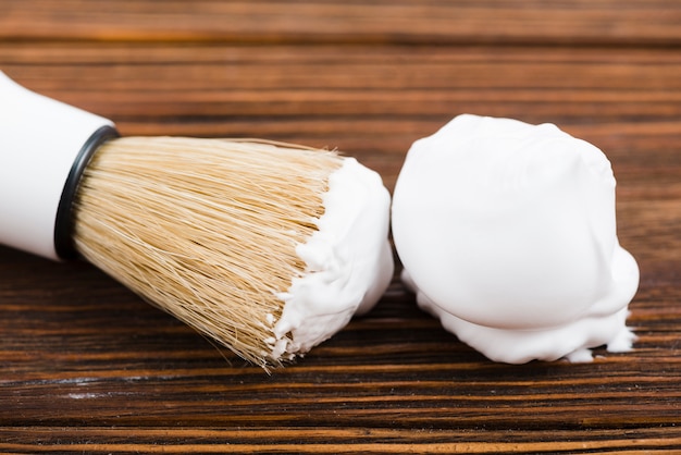 Free photo close-up of shaving foam with brush on wooden desk