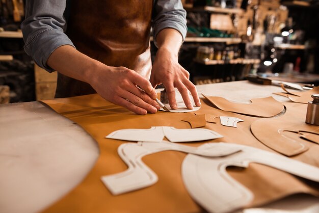 Close up of a shoemaker measuring and cutting leather