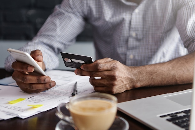 Close up shot of African man's hands holding mobile and credit card