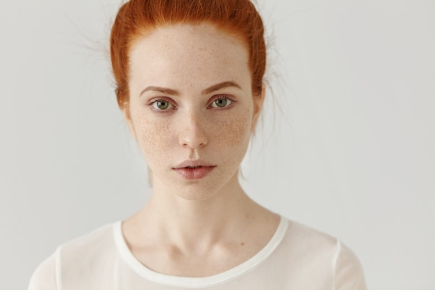 Free Photo close up shot of beautiful young redhead european female with extraordinary appearance relaxing indoors. good-looking pretty girl with ginger hair and freckles all over her face posing at white wall