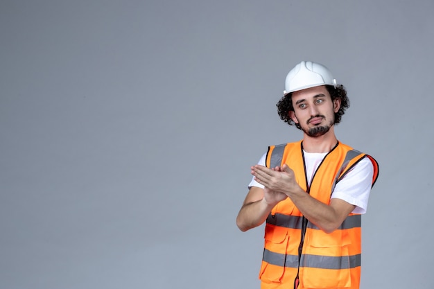 Close up shot of confident male architect in warning vest with safety helmet and applausing over gray wave wall