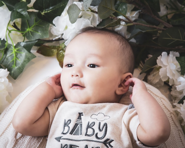 Close up shot of a cute Caucasian baby boy surrounded by flowers