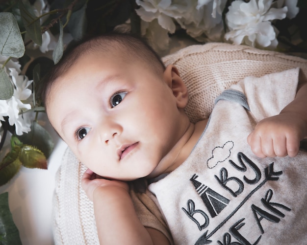 Free photo close up shot of a cute caucasian baby boy surrounded by flowers