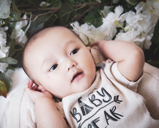 Close up shot of a cute Caucasian baby boy surrounded by flowers