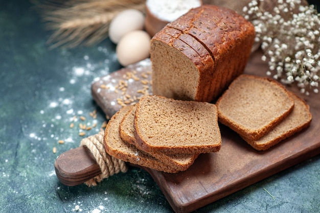 Close up shot of dietary black bread wheats on wooden cutting board spikes flower eggs flour in bowl on blue background