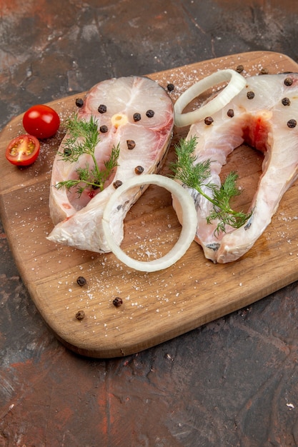 Free photo close up shot of fresh raw fishes and pepper onion greens tomatoes on wooden cutting board on mix color surface