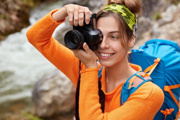 Close up shot of glad young Caucasian female tourist dressed in bright orange jumper