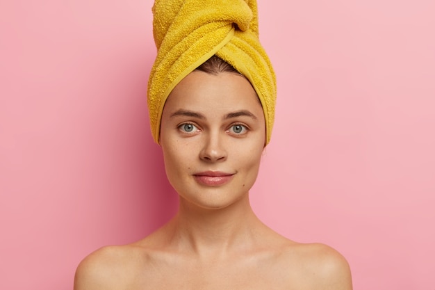 Free photo close up shot of gorgeous fresh european woman with towel on head, has clean face, healthy skin, stands shirtless, takes shower, going to apply makeup, has natural beauty. body care concept.