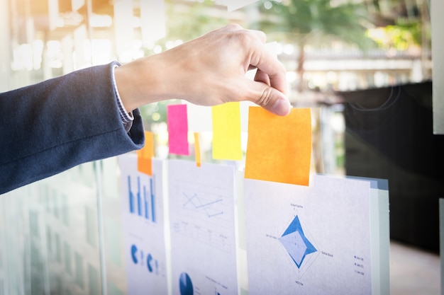 Free photo close up shot of hands of business man sticking adhesive notes on glass wall in office.